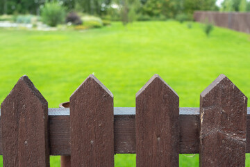 a wooden fence made of brown boards in the backyard. Green lawn in the background