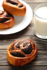 Bun with poppy seeds and glass of milk on brown wooden background. Vertical photo.