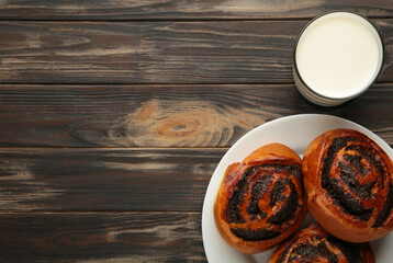 Bun with poppy seeds and glass of milk on brown wooden background.