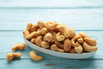 Cashew nuts on white plate on blue wooden background. Top view.