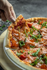 Woman hand hold Sliced pizza with salmon, red caviar, tomatoes and aragula. Traditional italian cuisine. vertical image. top view