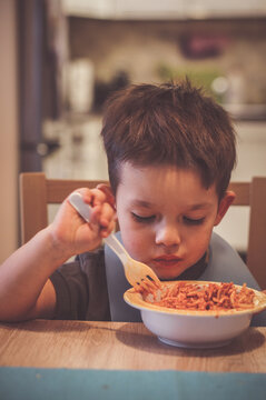 Vertical portrait of a little boy eating nuddles sitting at the table