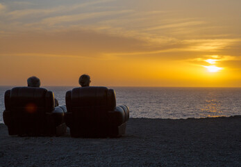 Two elderly people are sitting in armchairs and watching the sunset