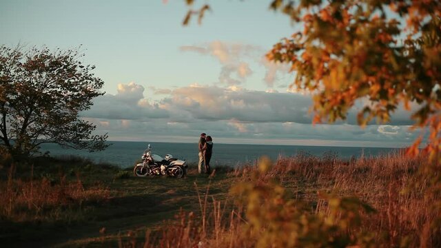 Young couple huggin and kissing on cliff edge on sunset.