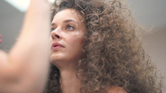 Close-up of a happy young woman with curly hair, she is being made up. They put shadows on her eyes, she looks away and smiles. High quality 4k footage