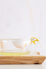 Shot of a transparent glass plate with a white egg separator with silicon holder under the handle. Egg separator with egg on a plate. Light wall on the background.