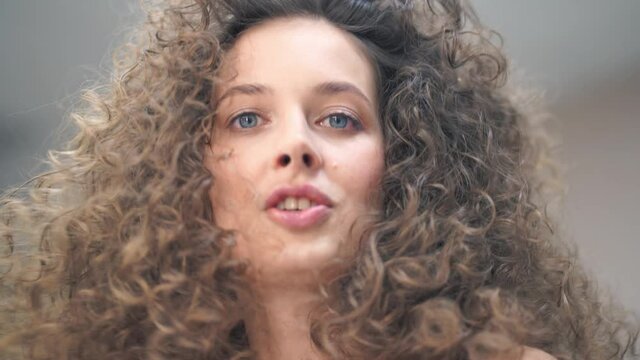 Close-up of a beautiful woman with curly hair, she looks at her hairstyle in the mirror and admires. High quality 4k footage