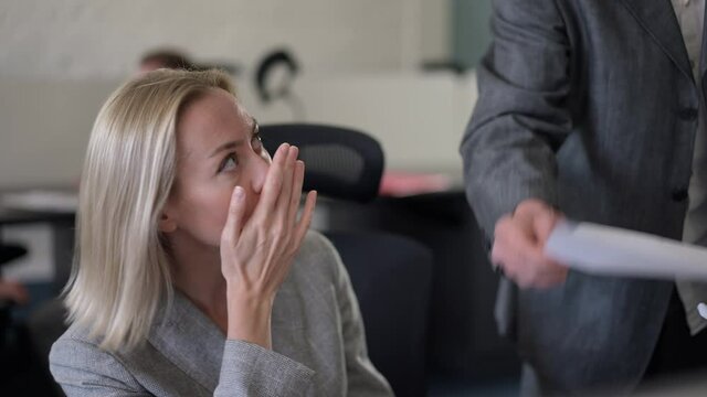 Portrait of anxious stressed Caucasian woman talking to unrecognizable boss passing paperwork yelling indoors. Worried beautiful female employee apologizing for mistake. Psychological abuse in office