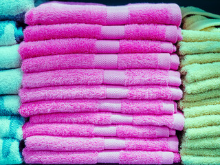 A stack of pink identical terry towels in the middle and turquoise and green towels on the sides