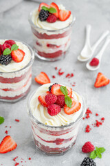 Red Velvet cake trifle with fresh berries in a glass jar on a gray concrete background. Dessert for Valentine's Day. Copy space.