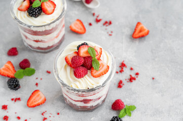 Red Velvet cake trifle with fresh berries in a glass jar on a gray concrete background. Dessert for Valentine's Day. Copy space.