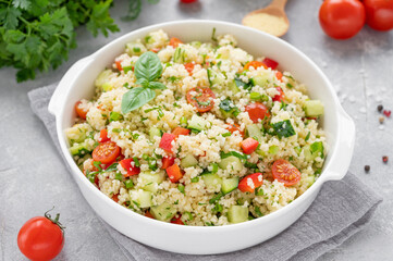 Tabbouleh salad. Couscous salad with fresh vegetables and herbs in a bowl on a gray concrete...