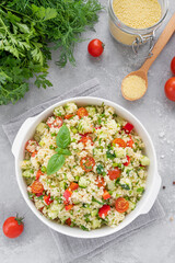 Tabbouleh salad. Couscous salad with fresh vegetables and herbs in a bowl on a gray concrete background. Copy space.