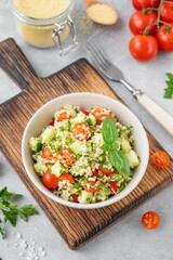 Tabbouleh salad. Couscous salad with fresh vegetables and herbs in a bowl on a gray concrete background. Copy space.