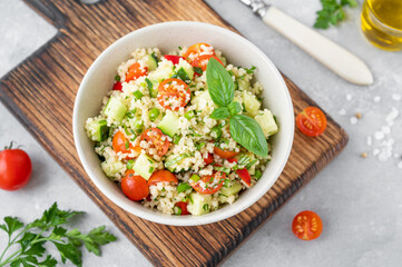 Tabbouleh salad. Couscous salad with fresh vegetables and herbs in a bowl on a gray concrete background. Copy space.