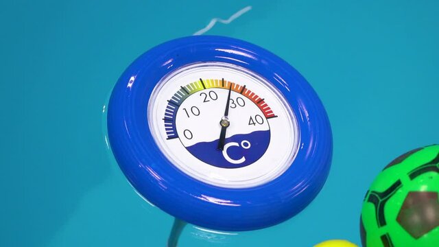 Thermometer is floating in a children's pool with blue water. 27 degrees Celsius. Slow motion. Close up view.
