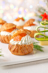 Festive savory profiteroles with salmon, cream cheese and dill on a white plate on a white background. Appetizer for Christmas and New Year. Selective focus.