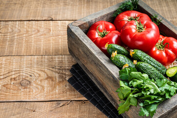 Fresh vegetables in a wooden box, red tomatoes, green cucumbers with herbs. Wooden background. Top view. Copy space