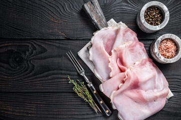 Sliced prosciutto ham on wooden board with herbs. Black wooden background. Top view. Copy space