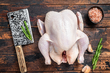 Whole chicken, raw poultry on a butchery table with meat cleaver. Dark Wooden background. Top view