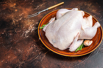 Chicken, raw poultry in a rustic plate with rosemary. Dark background. Top view. Copy space