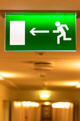 A bright green emergency evacuation sign with a directional arrow and a running figure hanging from...