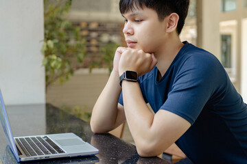 Online studying concept the man wearing dark blue shirt sitting on the wooden chair and trying to...