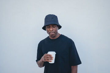 Young black man in street-style clothes holding his takeaway drink on a white background