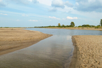 The coastal line of a sandy beach by the Baltic Sea on Sobieszewo island, Poland. There is a small pond separated from the sea by sand dunes. A bit of overcast. Few tress in the back. Calmness.