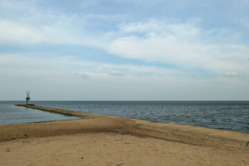 A view on Vistula Spit - an area where Vistula river is merging with Baltic Sea in Sobieszewo Island, Poland. The sea is gently waving, the river's surface is very calm. A bit of overcast. Few trees