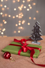 Christmas gift in a green kravtovoy package with a red bow on the background of a garland. Gift wrap