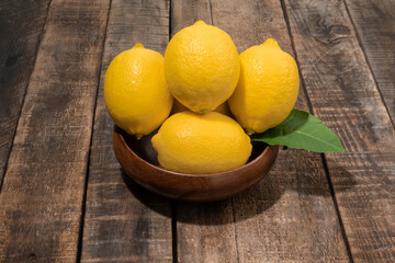 Lemon pile in bowl has leaves on wood background close up, top view, bio food concept.