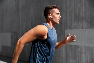 fitness, sport, training and lifestyle concept - young man in earphones running outdoors
