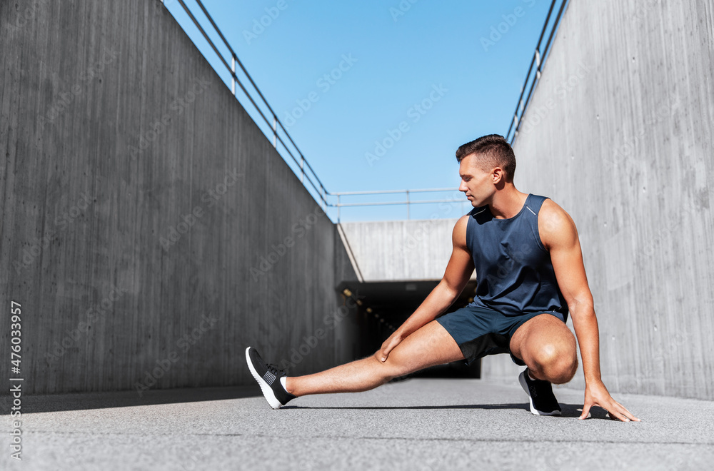 Wall mural fitness, sport and healthy lifestyle concept - man exercising and stretching leg outdoors