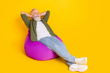 Photo of inspired mature man sit beanbag hands behind head sleep wear green shirt isolated yellow color background - Powered by Adobe