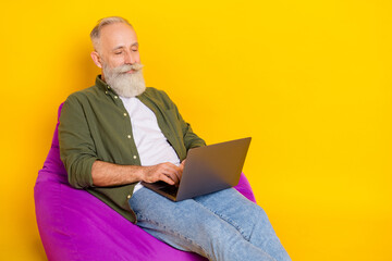 Photo of bearded programmer man sit beanbag hold pc typing wear green shirt isolated yellow color background