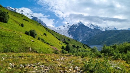 A panoramic view on the snow-capped peaks of Tetnuldi, Gistola and Lakutsia in the Greater Caucasus Mountain Range in Georgia, Svaneti Region. Hills with lush pastures, sharp peaks, wanderlust.