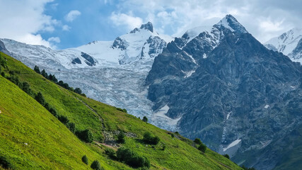 Fototapeta na wymiar A panoramic view on the snow-capped peak of Jangi-Tau(Dzhangi-Tau) in the Greater Caucasus Mountain Range in Georgia, Svaneti Region. Hills with lush pastures, sharp peaks, hiking vibes.