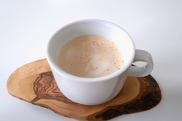 Latte with foam in a while cup served on a wooden coaster over the white table