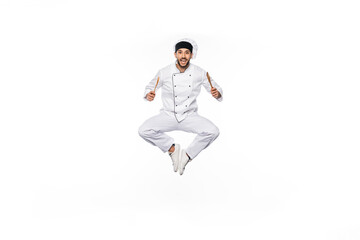 Fototapeta na wymiar cheerful chef in hat and uniform jumping and holding wooden spatula and spoon isolated on white.