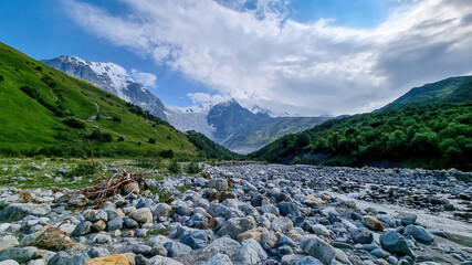 River Adishischala flowing down the a valley. View on Adishi Glacier and on the snow-capped peaks of Tetnuldi, Gistola and Lakutsia in the Greater Caucasus Mountain Range in Georgia, Svaneti Region.