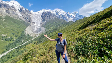 A woman on a hiking trail with a panoramic view on the snow-capped peaks of Tetnuldi, Gistola, Lakutsia and the Adishi Glacier in the Greater Caucasus Mountain Range in Georgia,Svaneti Region.