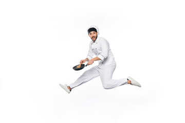 happy chef in hat and uniform jumping and holding frying pan with wooden spatula isolated on white.