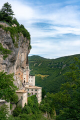 Fototapeta na wymiar Monastery church perched on rocky cliff surrounded by forest, Madonna della Corona, Italy