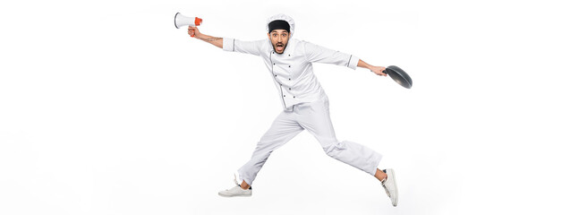 Fototapeta na wymiar surprised chef in hat and uniform levitating while holding frying pan and megaphone isolated on white, banner.