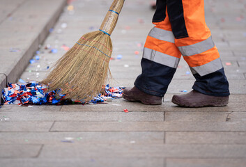 A janitor with a broomstick removes bright colorful confetti from the side of a city street after a...