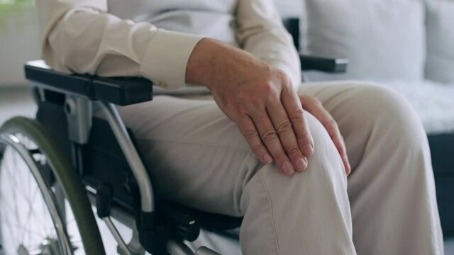 Man in wheelchair rubbing injured knee, rehabilitation after injury, arthritis