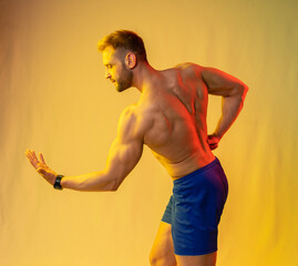 muscular man in blue shorts posing shows, straining his muscles. yellow and red highlights on the...