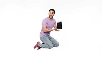 amazed man in jeans and purple t-shirt levitating while holding digital tablet on white.