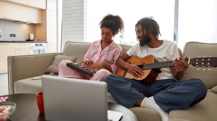 Young black couple playing music on sofa at home